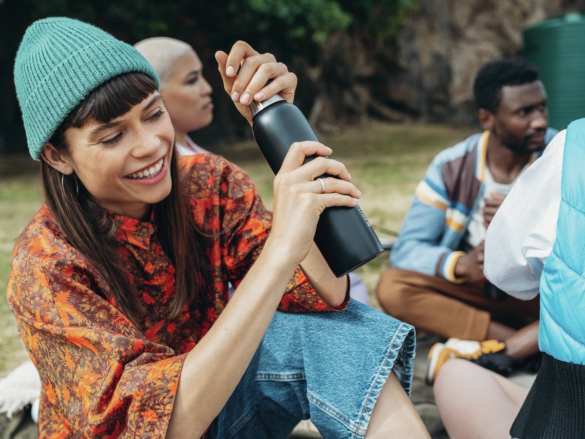 Black BRITA sodaTRIO stainless steel bottle being held outdoors in a group setting.